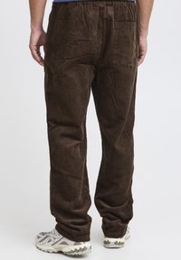 Brown corduroy pants with vertical ribbing, featuring an elastic waistband and a back pocket, paired with gray and beige sneakers.