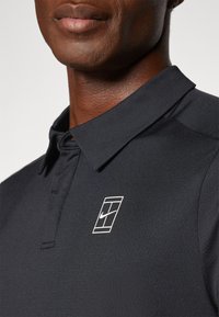 Black polo shirt with short collar, featuring a white Nike logo on the left chest. Made from textured fabric with a sleek, modern design.
