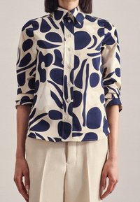 Button-up shirt made of cotton with a cream base and abstract navy blue shapes, featuring a classic collar and rolled-up sleeves.
