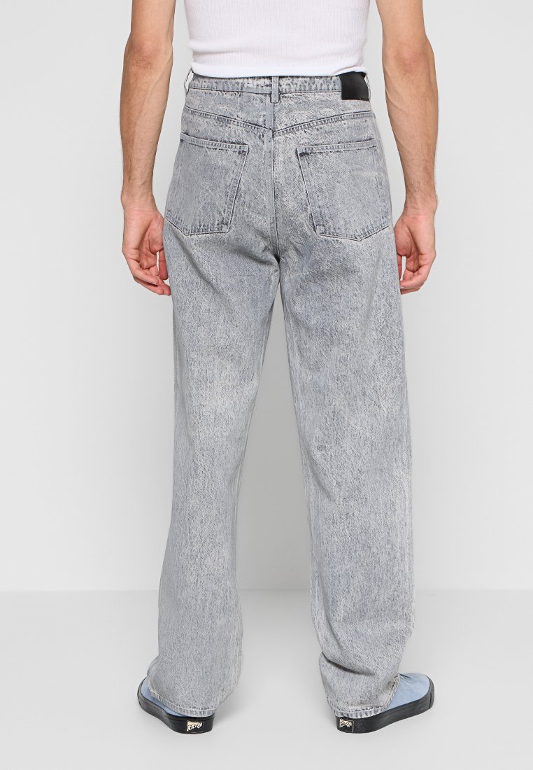 Lichtgrijze, loszittende jeans met een vervaagde wassing, vijf zakken en een rechte pijp. Draag ze met zwarte instapschoenen.