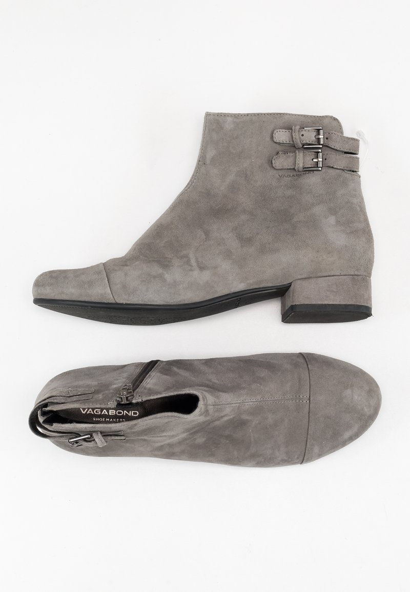 Bottes cheville en daim gris avec talons bas, fermeture éclair latérale, deux sangles à boucles et bout rond, posées à plat sur un fond blanc.