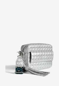 Metāliska sudraba plecu soma ar izšūtu rakstu, priekšējo kabatu ar atloku, fringing detaļām un noņemamu siksnu ar zilo un melno akcentu.