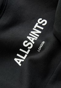 Sweat-shirt noir arborant un lettrage blanc audacieux "ALLSAINTS" et "LONDON." Tissu texturé avec une finition lisse, col rond.