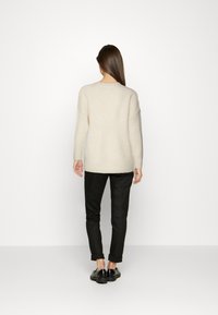 Pulover crem, cu mâneci lungi și largi, cu guler rotund, asortat cu pantaloni negri slim-fit și pantofi negri. Design simplu.