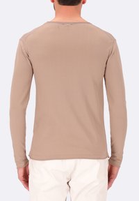 Camicia beige a maniche lunghe con collo rotondo, texture liscia, design aderente e dettagli di cucitura minimi sulle spalle e sulle maniche.