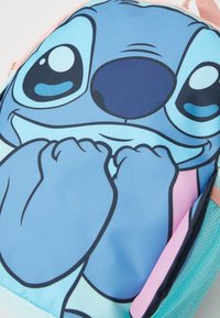 Mochila com grande rosto de personagem de desenho animado azul, olhos grandes e mãos perto da boca, em cores azul pastel, rosa e verde-água.