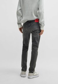 Jeans in denim grigio scuro con vestibilità slim, dotati di una patch rossa sul retro, design a cinque tasche e dettagli sfumati sottili.