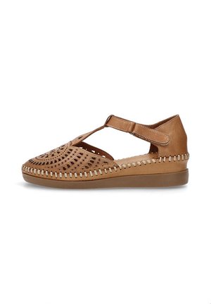 Zapato de cuero marrón claro con diseño perforado, correa ajustable y costura decorativa a lo largo de la suela. Suela plana para mayor comodidad.