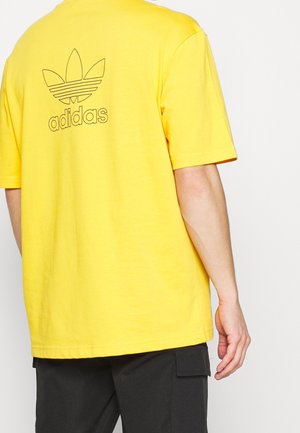 Geel katoenen T-shirt met korte mouwen. Voorzien van een zwart Adidas-logo en trefoil-ontwerp op de achterkant. Rechte snit en minimale details.
