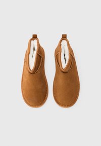 Brune fløyelslippere med hvitt fleece-fôr, sett ovenfra på en enkel hvit bakgrunn.