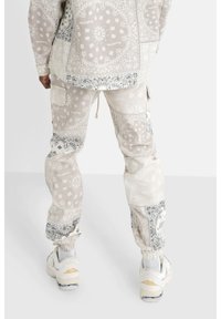 Světle šedý outfit s vzorem bandany, s volným střihem a elastickými manžetami. V kombinaci s objemnými bílými teniskami.
