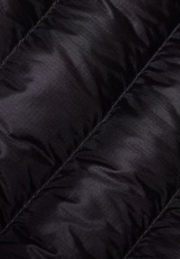 Nærbillede af sort kviltet stof med diagonale sømme og et subtilt gittermønster på overfladen.