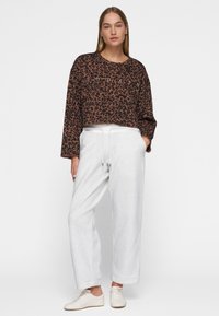 Sweatshirt cropped à motif léopard marron avec des manches longues ; associé à un pantalon de jogging gris clair avec une taille à cordon. Des baskets blanches complètent le look.