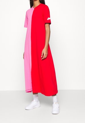 Krátké šaty s růžovou a červenou polovinu, vyrobené z bavlny. Mají kulatý výstřih a logo Nike na rukávu. Nošeny s bílými teniskami.