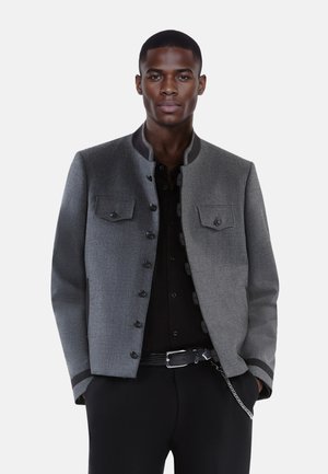 Graue strukturierte Jacke mit rundem Kragen, vorderen Knöpfen und zwei Brusttaschen. Schwarze Akzente am Kragen und an den Manschetten.