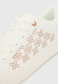 Sneaker bianca con design con lacci, motivo a stella ritagliato in rosa chiaro e suola in gomma texture con accento bronzo all'occhiello.