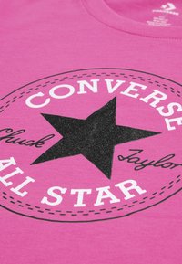 Maglietta di cotone rosa con logo a stella nera, con la scritta "CONVERSE" sopra e "ALL STAR" sotto, evidenziata da testo bianco e bordo cucito.