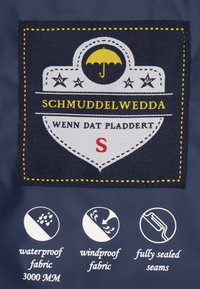 Etiqueta de tela en color azul marino con un diseño de escudo blanco que incluye un icono de paraguas amarillo, el texto "SCHMUDDELWEDDA" y símbolos de cuidado para impermeabilidad.