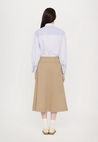 Raitapaita sinivalkoinen, jossa on käärittävät hihat, yhdistettynä beigeksi polven yli ulottuvaan hameeseen, jossa on muotoiltu vyötärö ja sileä pinta.