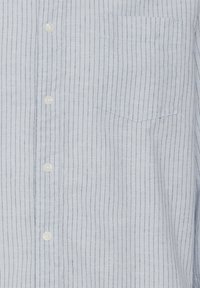 Camicia azzurra chiara in misto lino, caratterizzata da strisce verticali navy, una tasca sul petto e bottoni bianchi. Tessuto testurizzato.