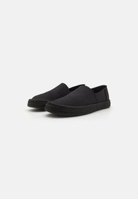 Sorte kanvas slip-on sko med en vevd svart taustøvel, rund tå og elastiske sidepaneler for enkel påkledning. Minimalistisk design.