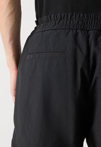 Shorts noirs avec taille élastique, dotés d'une poche au dos. Le matériau semble léger avec une texture lisse. Design simple et sans motifs.