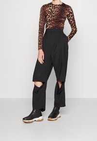 Person som bär en långärmad topp med leopardmönster, svarta vida byxor med knäöppningar och svarta ankelstövlar med vita sulor.