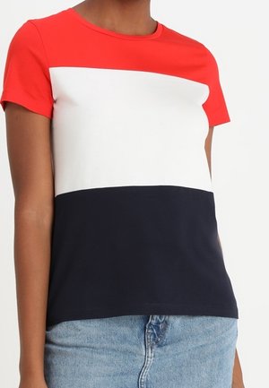 Femme portant un T-shirt à manches courtes avec des blocs de couleur rouge, blanc et bleu marine en sections horizontales et un jean en denim bleu clair.
