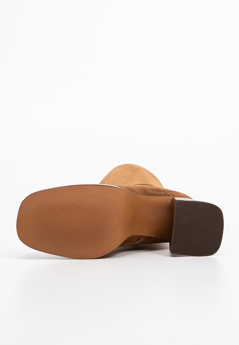 Bottine en daim brun avec un talon carré et une semelle en caoutchouc texturé. La semelle est de couleur marron clair, contrastant avec le matériau supérieur.