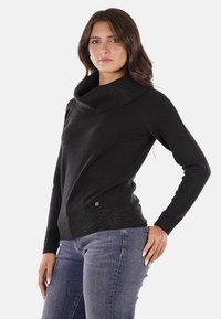 Maglione nero con colletto a pipistrello, maniche lunghe, tessuto testurizzato e design aderente. Presenta una leggera lucentezza sul colletto e sull'orlo.
