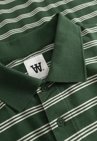 Polo vert foncé avec des rayures horizontales blanches, deux boutons et un col plié.