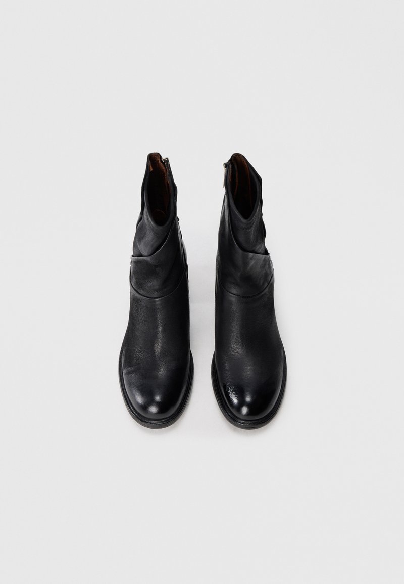 Une paire de bottines en cuir noir avec des fermetures éclair sur les côtés, vues de dessus sur un fond blanc uni.
