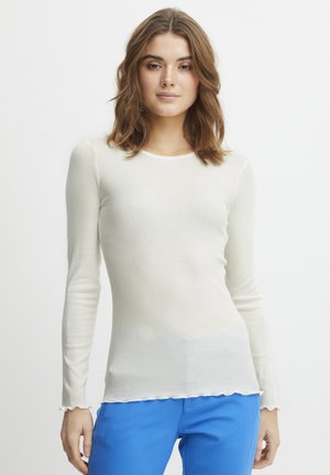 Weißes, geripptes Langarmoberteil mit gewelltem Saum und Kragen. Der Stoff hat eine weiche Textur und wird mit lebhaft blauen Hosen kombiniert.