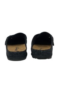 Scarpe slip-on nere in feltro con superficie testurizzata, aperte sul retro e con una soletta color cuoio. Presentano una suola piatta in gomma e accenti di cucitura decorativa.