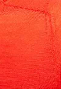 Tissu tricoté rouge avec une texture fine et lisse. Présente un bord côtelé sur un côté et un motif finement tissé sur l'ensemble.