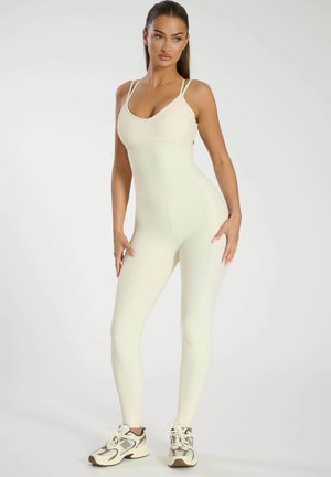 Mono de canalé color crema con tirantes finos, silueta ajustada y costuras en contraste. Combinado con zapatillas deportivas en tonos neutros.