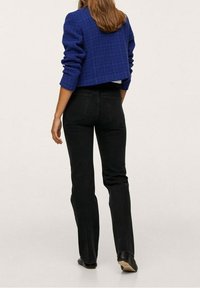 Afgekorte blauwe textuurjack over zwarte jeans. De outfit heeft een eenvoudig ontwerp met een getailleerde snit en zwarte schoenen.
