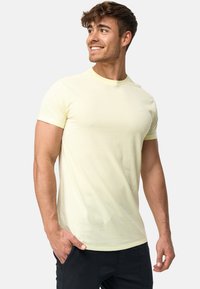 Camiseta de manga corta de color amarillo claro con un cuello redondo y un diseño ajustado. Cuenta con un pequeño logo en la parte izquierda del pecho.