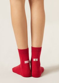 Chaussettes rouges à la cheville avec une texture côtelée, comportant une petite étiquette avec une illustration et le texte « Warm Wish » au dos.
