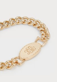 Zelta ķēdes rokassprādze ar ovālu aizdari, kas iegravēta ar iniciāļiem, gluda metāla apdare, savienotas saites un pulēta virsma.