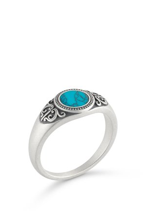 Zilveren ring met een ronde turkooizen steen in het midden, met zwarte decoratieve krullen rond de steen op een witte achtergrond.