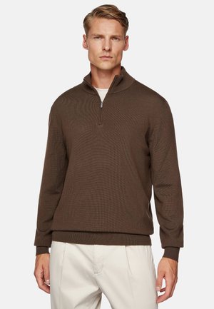 Maglione zip-up marrone con texture a coste e colletto alto. Presenta maniche lunghe e una vestibilità comoda, abbinato a pantaloni di colore chiaro.