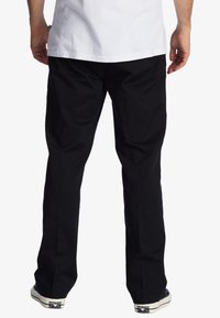 Black cotton pants with a relaxed fit, featuring a smooth texture. Worn with a white t-shirt and canvas shoes, showing a simple design.
