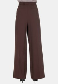 Pantaloni ampi in tessuto marrone scuro con una texture liscia. Presentano una vita alta e tasche anteriori per praticità.