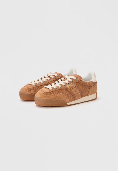 Sneaker in suede marrone con tessuto perforato, lacci crema e suole in gomma testurizzata. Presenta righe laterali e un piccolo logo sulla linguetta.