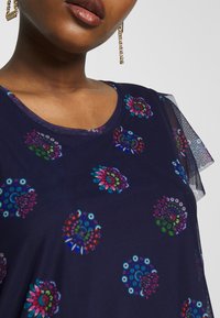 Navy short-sleeve top with floral patterns in vibrant colors. Features a round neckline and sheer mesh detail on the sleeves.