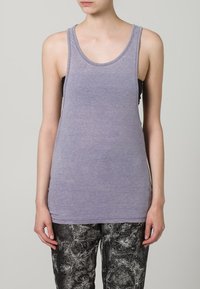 Lilla ermeløs tanktop laget av mykt stoff. Har en jevn tekstur, rund halsutskjæring og en slank passform, kombinert med mønstrede bukser.