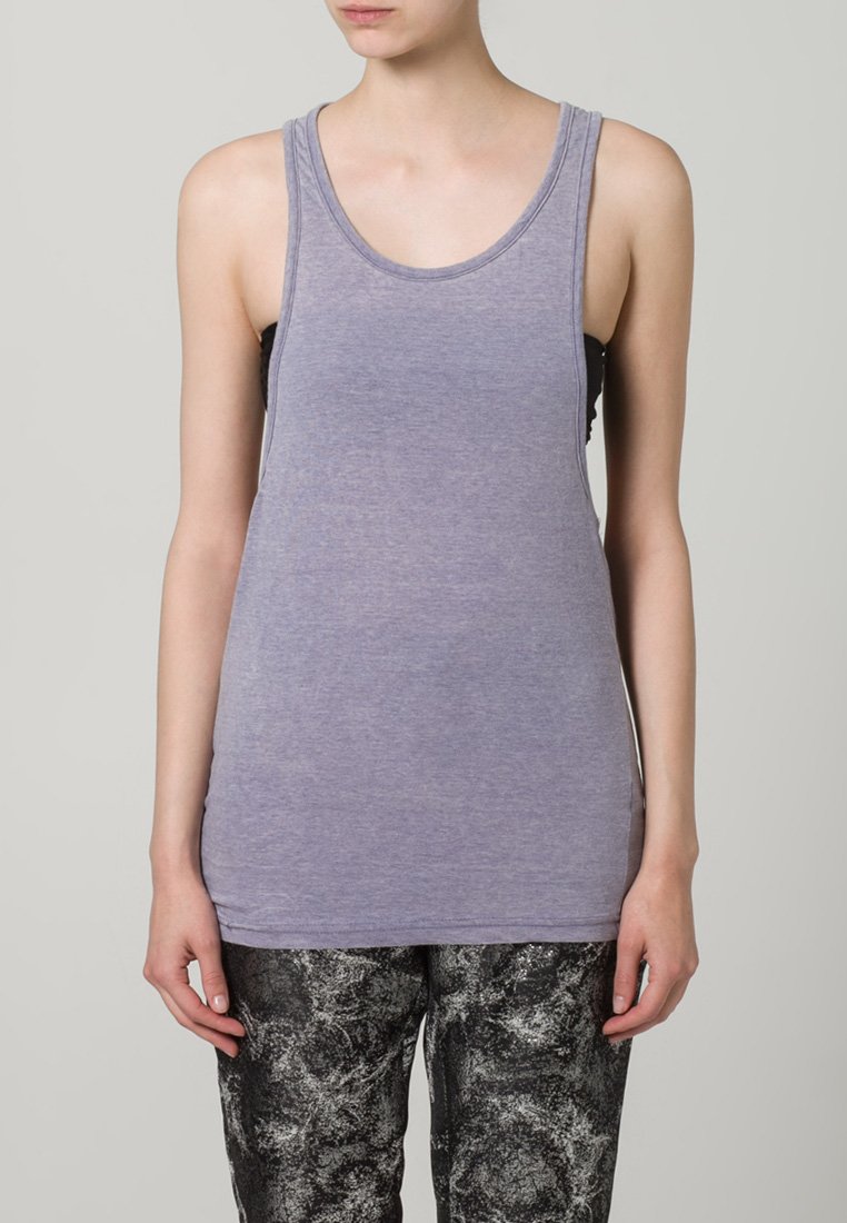 Lilla ermeløs tanktop laget av mykt stoff. Har en jevn tekstur, rund halsutskjæring og en slank passform, kombinert med mønstrede bukser.