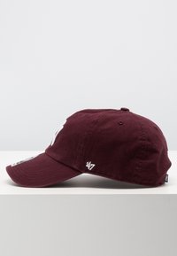Gorra de béisbol color burdeos con visera curva, hecha de algodón. Presenta un logo bordado y un acento en el lado, con tejido texturizado.