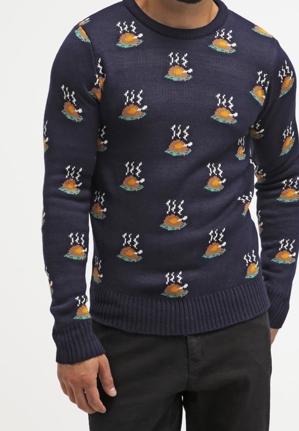 Pull bleu marine avec motifs répétés de dindes rôties fumantes, porté par une personne en pantalon noir, cadré au niveau du cou et des cuisses.
